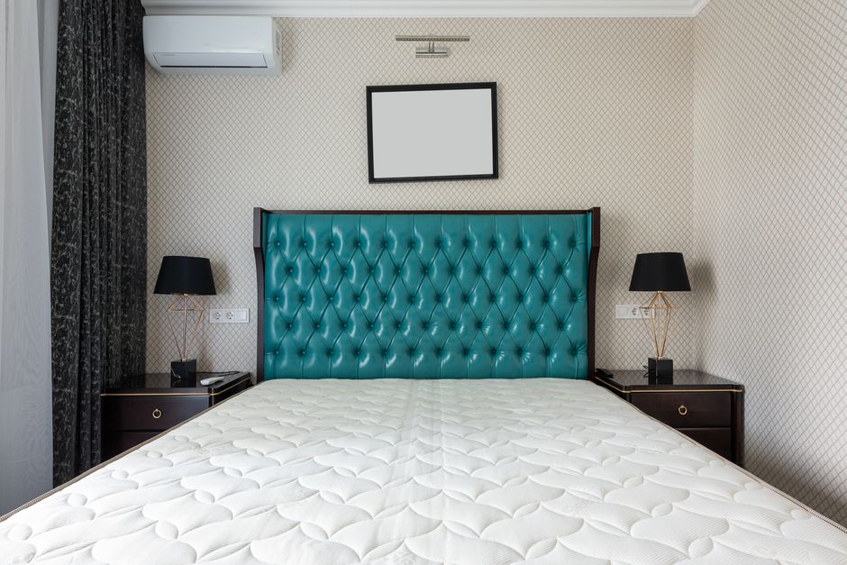 A modern bedroom featuring a grey upholstered bed with a white mattress, positioned against a textured grey accent wall with vertical paneling. On each side of the bed are matching grey bedside tables